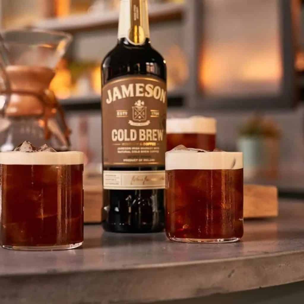 Bottle of Jameson Cold Brew Whiskey with rocks glasses filled with cocktails topped with cream